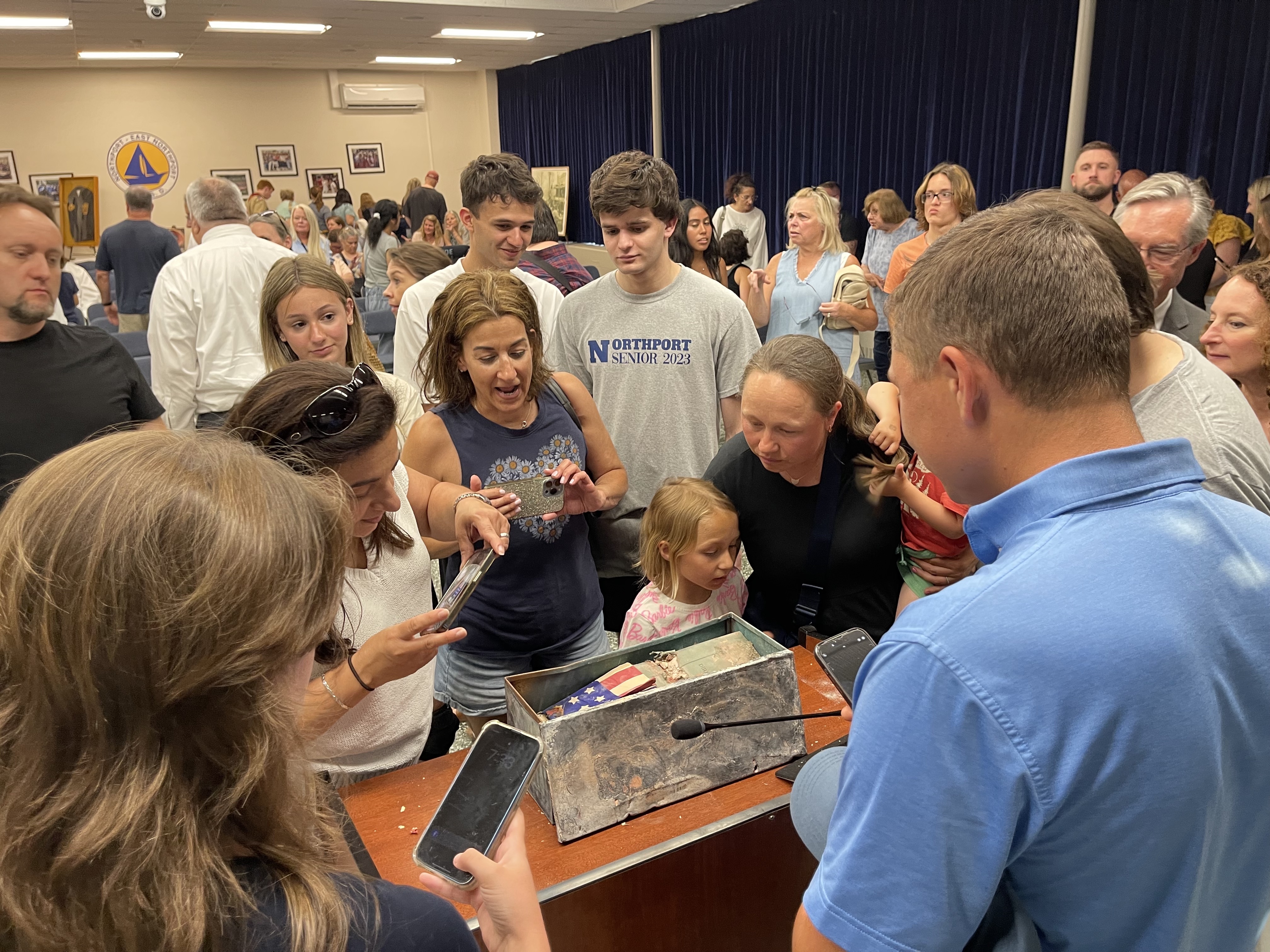Audience members take photos of the time capsule, and its contents, at the June 20 BOE meeting.