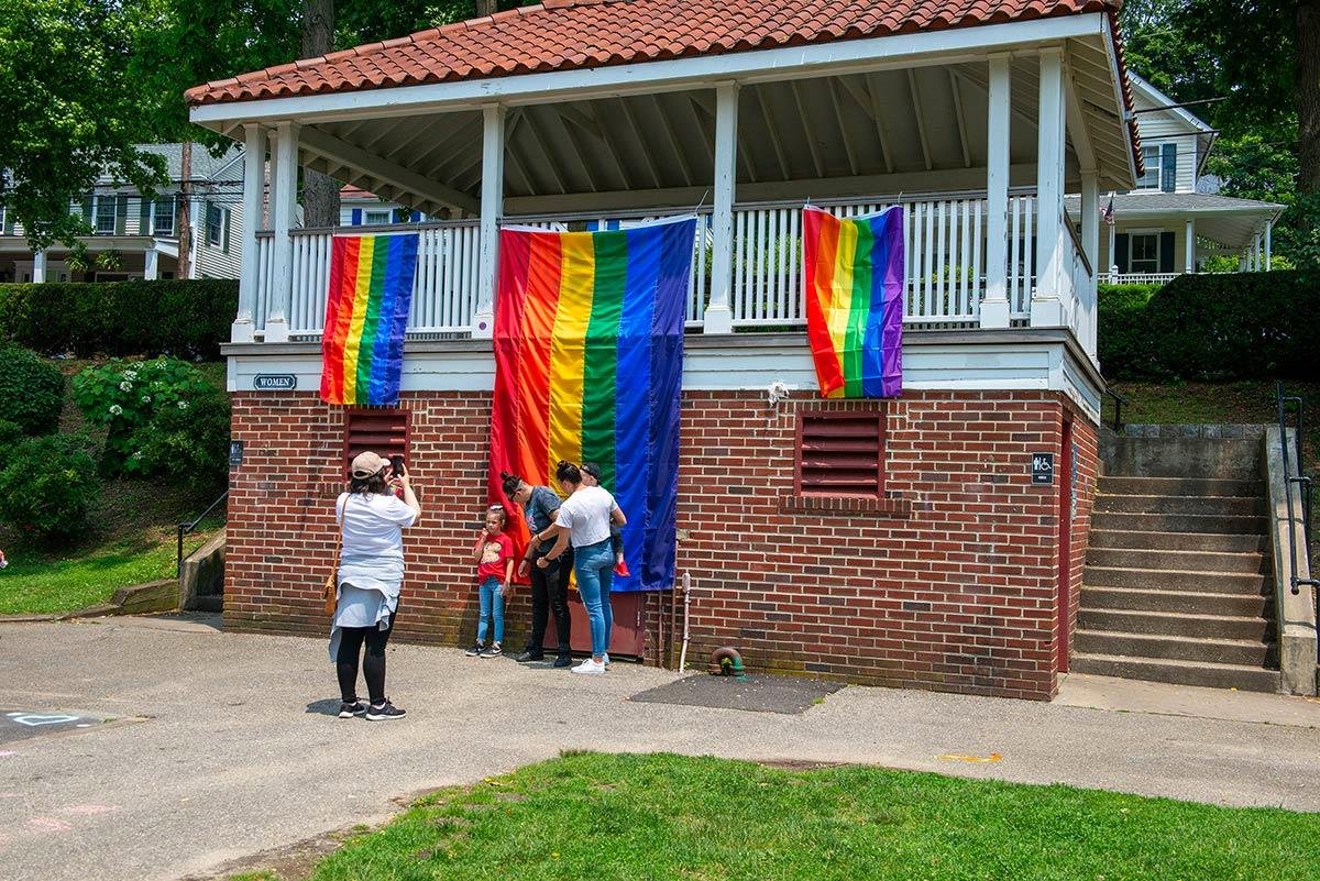 A family poses in front of three of many Pride flags hanging in Northport Village Park.