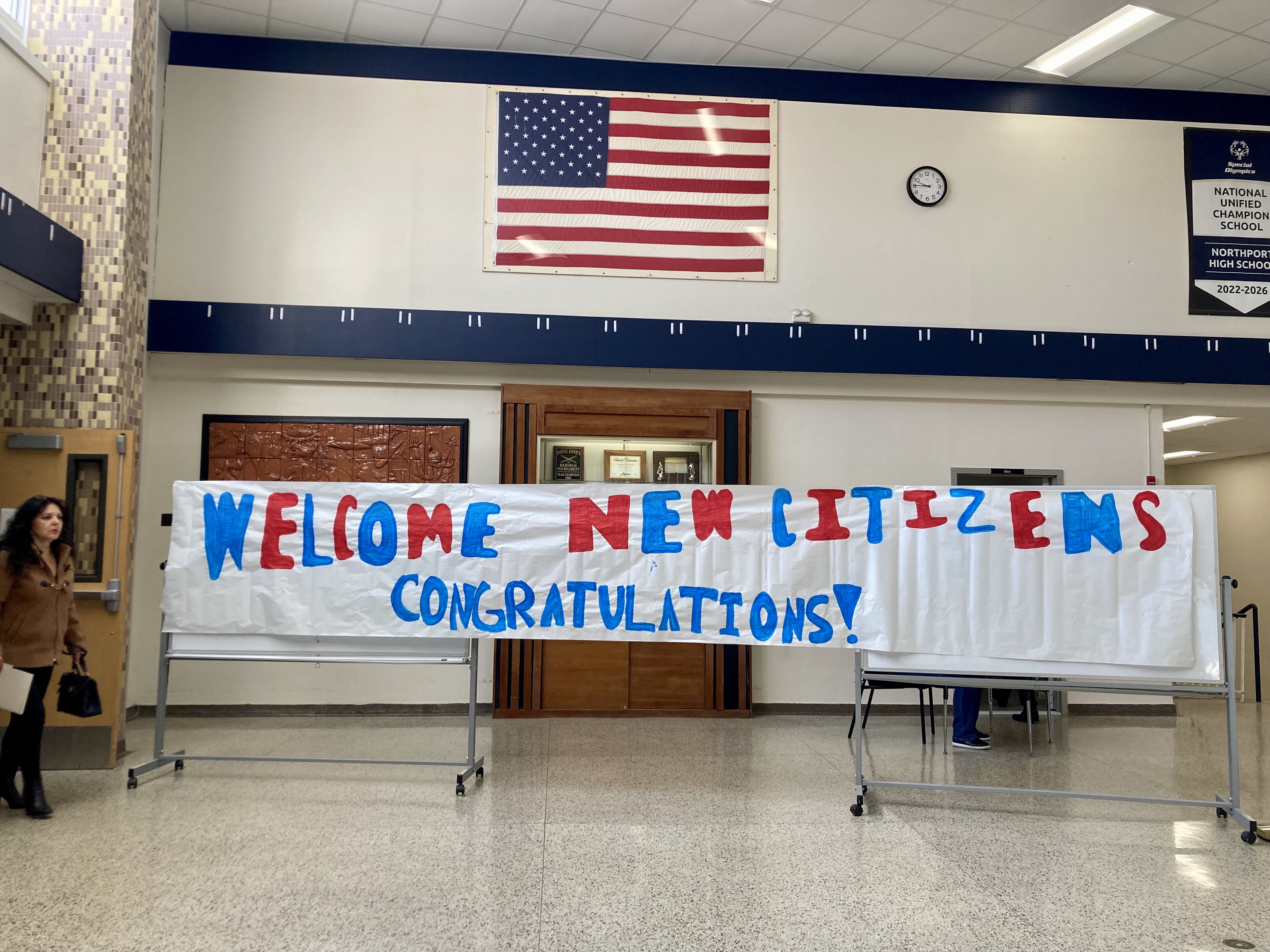 A woman awaiting the beginning of a naturalization ceremony at Northport High School walks past a banner created by students to welcome 75 candidates as new US citizens. 