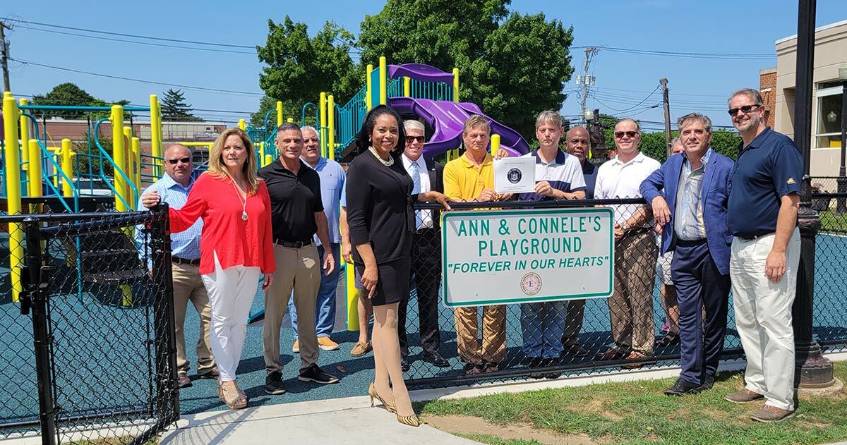 Leonard and Allen Pabo (center), brothers of Ann Pabo, with members of the Walsh family, representatives from the Town of Huntington, and other government representatives at a ribbon-cutting last week, rededicating the renovated playground to their sister and nephew, who were killed 12 years ago in a murder-suicide.