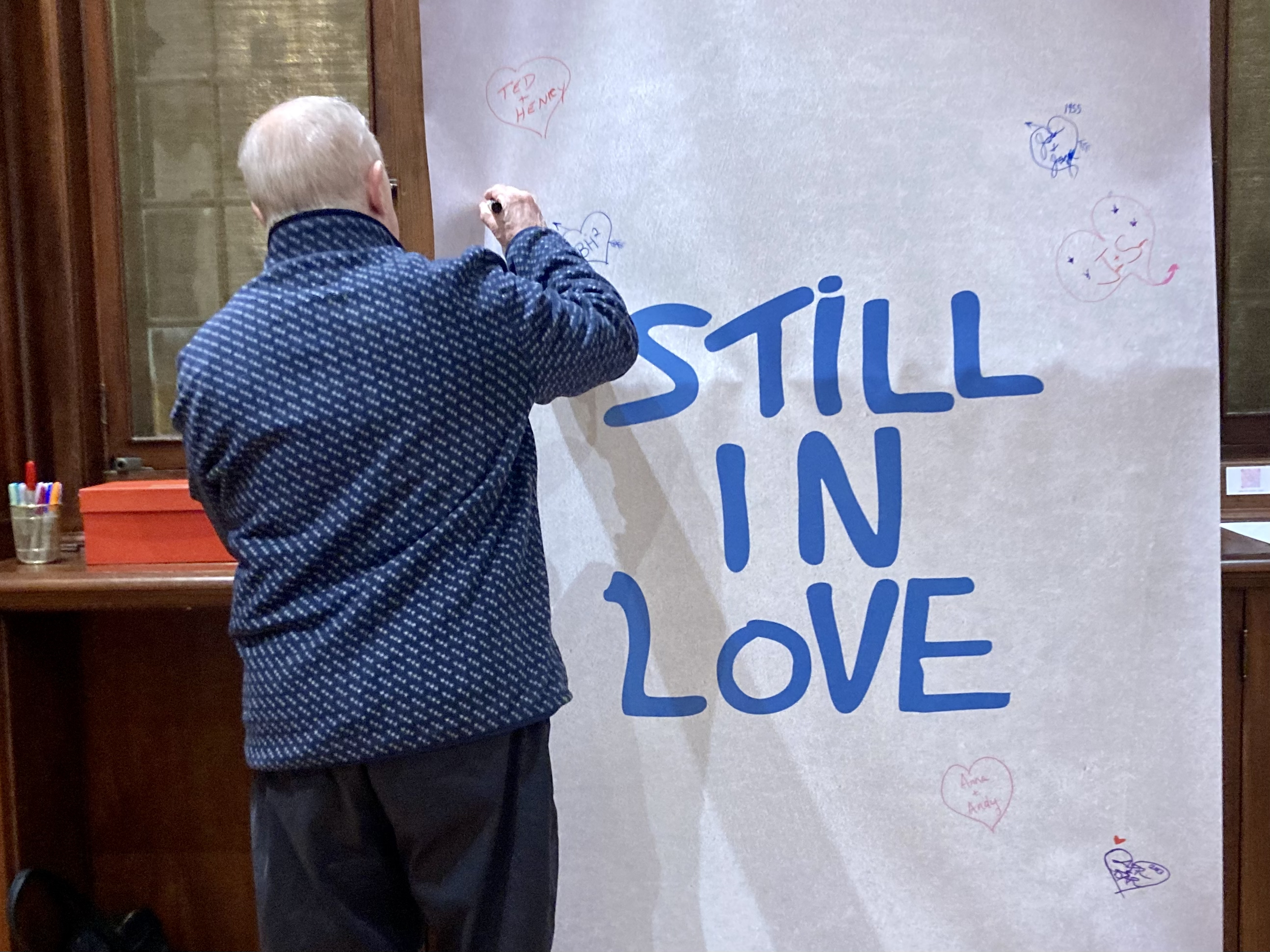 A guest at the Northport Historical Society’s opening reception for its “Still in Love” exhibit leaves his mark on a work in progress. Also in progress is a documentary exploring the origins of the iconic Still in Love street art on Bayview Avenue in Northport Village.  